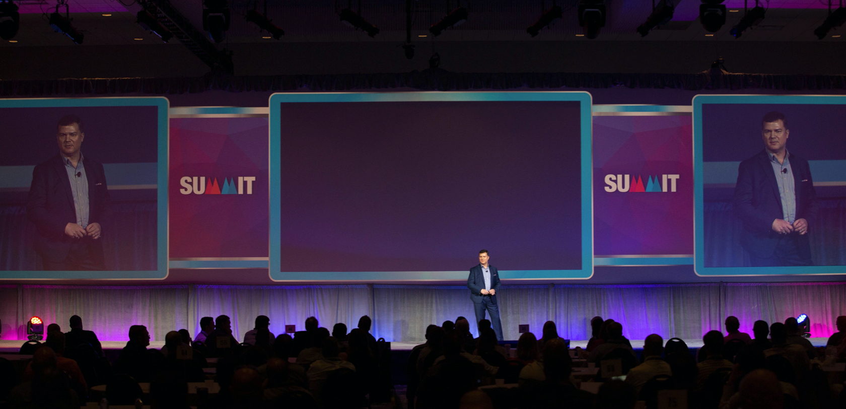Robert Cujo Teschner speaking on stage at a summit conference with large audience